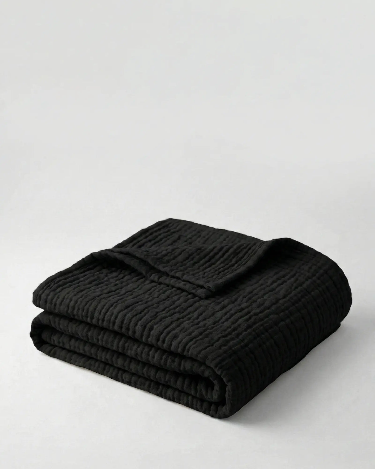 Muslin Blanket in Black draped over a bed