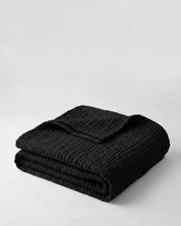 Muslin Blanket in Black draped over a bed