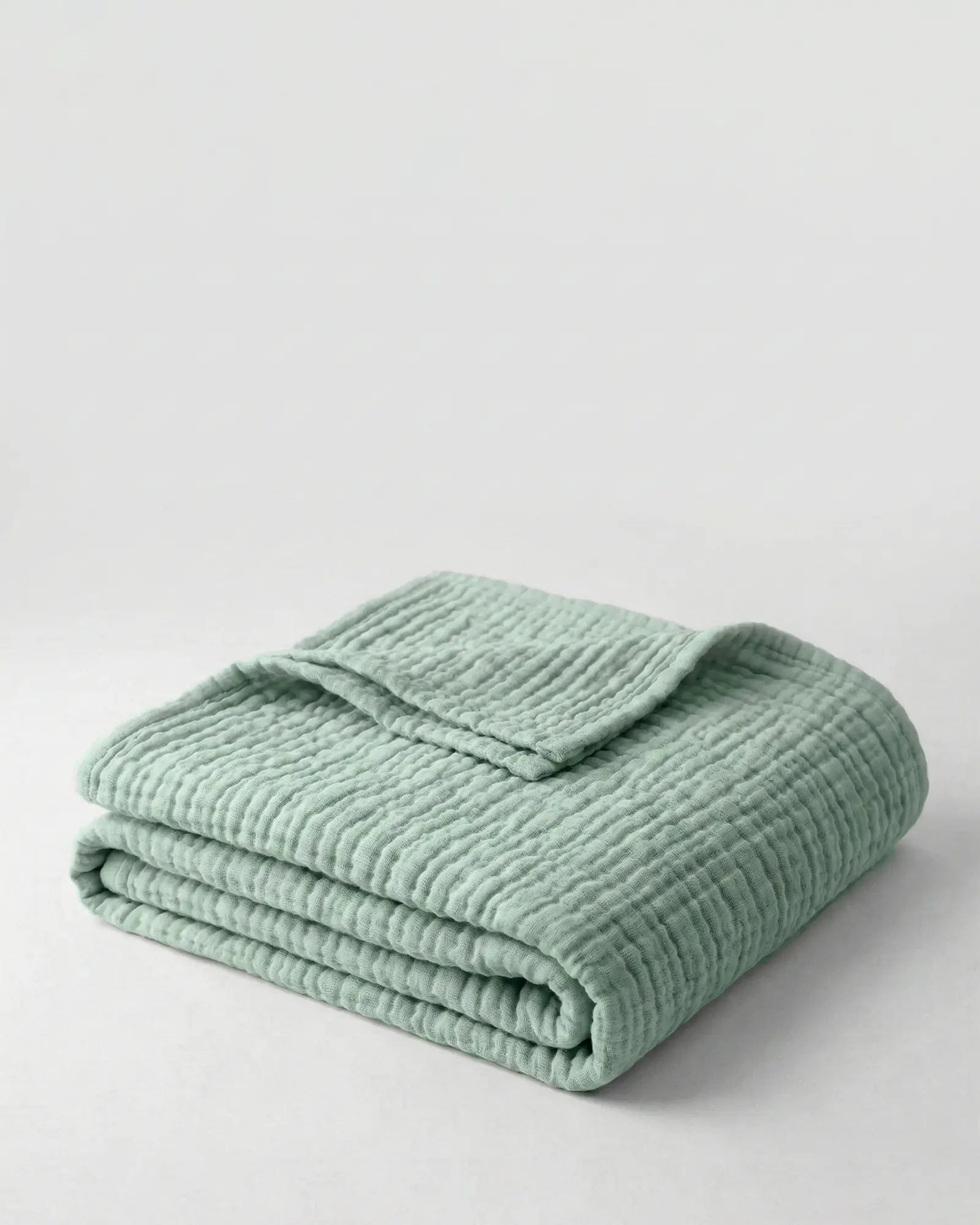 Muslin Blanket in Green draped over a bed